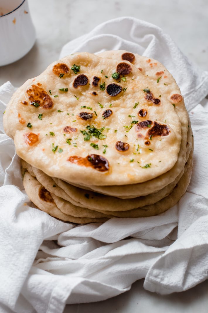 stack of garlic naan brushed with garlic butter on flour sack towel